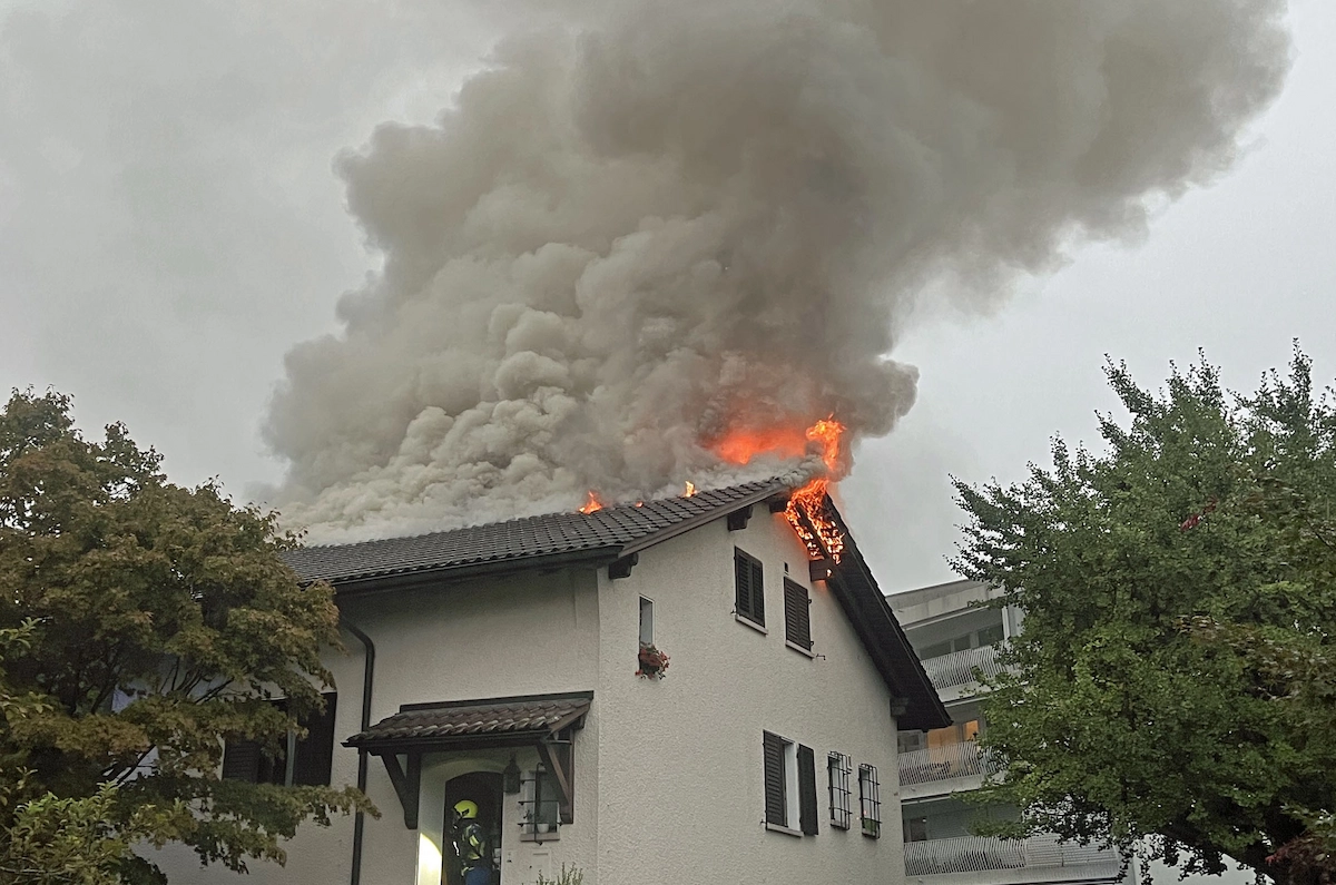 Dach eines Wohnhauses steht in Flammen, dichter Rauch steigt auf