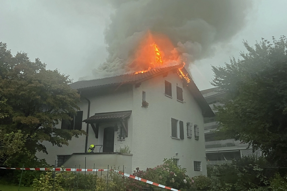 Lodernde Flammen am Dachfirst eines Wohnhauses, Feuerwehr vor Ort